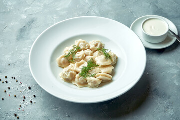 Classic homemade dumplings with minced meat and sour cream in a white plate on a gray background