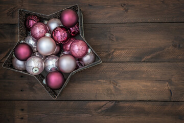Star-shaped bowl filled with pink and silver christmas baubles. On wooden background with copy space.
