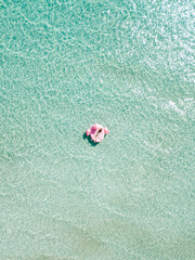 Aerial view of young woman in bikini lying on inflatable plastic pink flamingo in azure sea water, swim, sun bathe, relax on beach Punta Prosciutto, Italian Maldives Puglia Italy. Summer time vacation