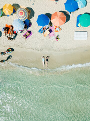 PUGLIA, ITALY - SEPTEMBER 06, 2018: Aerial view two young girls in swimwear lie on sand beach Punta Prosciutto Italian Maldives. Summer vacation. People sun bathe swim relax under umbrellas. Sea waves