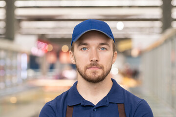 Head and shoulders portrait of handsome young man working in supermarket standing in aisle looking at camera