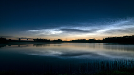 night landscape with white silver clouds over the lake, blurred foreground, charming cloud reflections in the lake water, summer night