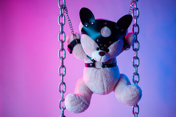 toy bear dressed in leather belts harness accessory for BDSM games on a dark background in neon light