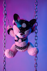 toy bear dressed in leather belts harness accessory for BDSM games on a dark background in neon...
