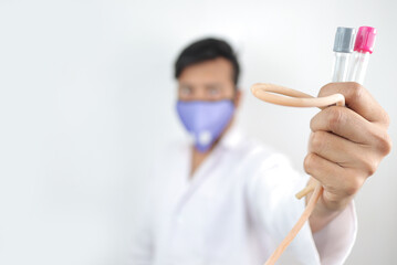 a medical professional in white coat and protective mask holding vials and tourniquet in hand with selective focus in hand with blurred background