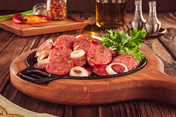 Sliced smoked calabrese sausage with onion in a wooden background - Brazilian appetizer