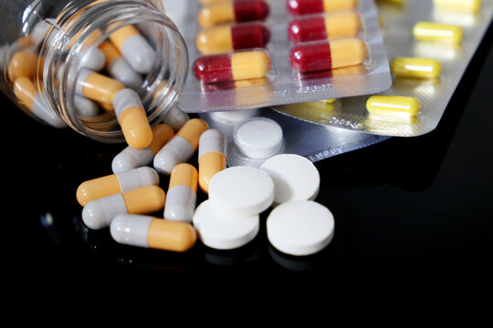 Pills on a dark glass table, variation of medication in capsules and tablets scattered from a bottle. Concept of pharmacy, antibiotics, vitamins