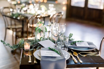 A beautiful table decorated with candles, wine glasses, plate with green garland, gray napkins 