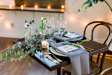 Beautiful table design at a wedding reception with napkins, wine glasses, and greenery in vases and candles on a table. 