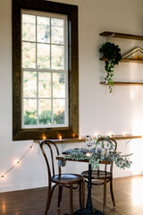 A table with two chairs against a window, decorated with green garland