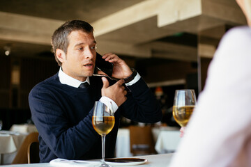 Handsome businessman dressed in the suit drinking wine. Businessman talking to the phone..