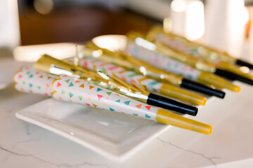 Festive party horns in gold and colorful colors lay on a square white plate at a fun party and event. 