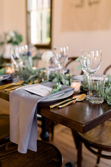 Beautiful wedding table setting with long draping napkins, gold silverware, elegant glass wine glasses and lots of lush greenery. 