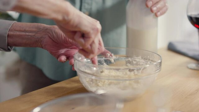 Handheld close up shot of unrecognizable elderly people making dough for cookies in kitchen