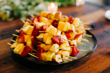 Skewers of pineapple and strawberry on a wood table.