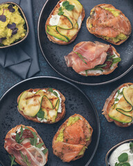 Assorted bruschetta with various toppings on a dark plates on dark background. Appetizing bruschetta. Mediterranean cuisine. Top view