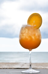 Vertical view, Orange juice in a tall glass with the blurred sea background.