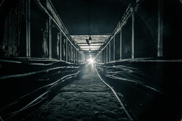 Dark concrete cable tunnel is illuminated by LED flashlight light in the end.