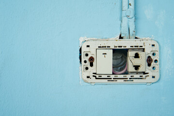 Power switch and defective plug, dirty and dangerous, No maintenance electric plug, on blue pastel wall.
