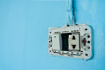 Power switch and defective plug, dirty and dangerous, No maintenance electric plug, on blue pastel wall.