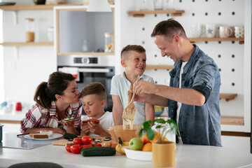 Mother and father making breakfast with sons. Young family preparing delicious food in kitchen..