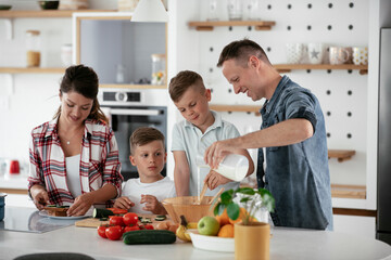 Mother and father making breakfast with sons. Young family preparing delicious food in kitchen..