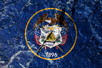 The national flag of the State of Utah USA on a blue background with a seal in the center, surrounded by a gold border with a bald eagle with arrows in its talons painted on the mountain wall.