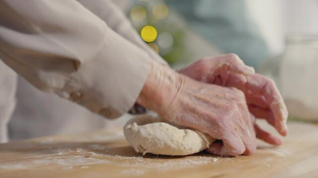 Handheld close up shot of unrecognizable elderly woman kneading dough in kitchen