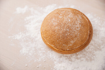 White round loaf of bread lies on table with flour, top view