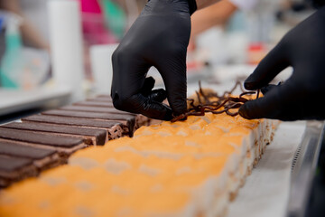 Close-up of chef hands preparing cakes and desserts covered with chocolate glaze