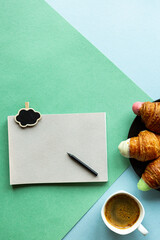 Business planning concept. Notepad, pencil, croissant and coffee on a green-blue background.