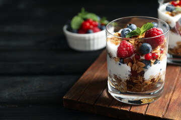 Yummy dessert with granola, yogurt and berries on dark wooden table, space for text