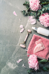 Facial roller, gua sha massager, oil bottle, towel, pink peonies on marble background. Copy space....