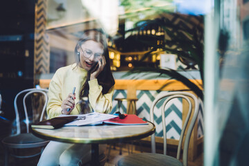 Young woman talking on phone while working in cafe