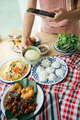 Woman hand taking picture of Isan food with smartphone.