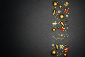 A band of flat lay golden christmas ornaments on a black stone plate. Spanish text "Feliz Navidad" (Merry Christmas) inbetween. Copy space.