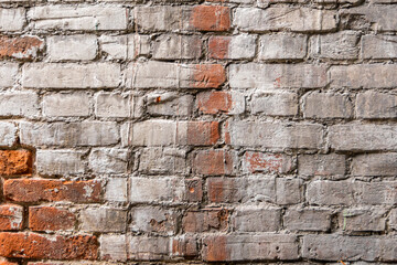 Old, antique wall of red destroyed bricks. White plaster was applied over the brickwork. The plaster is cracked