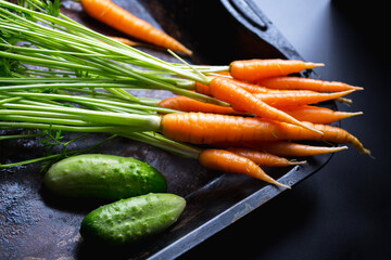 young carrots with cucumbers on a dark background, fresh vegetables from the garden