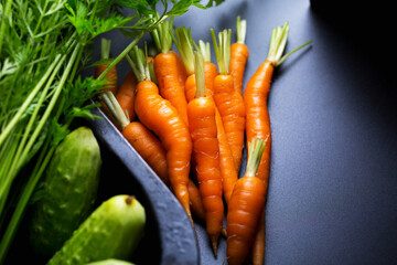 young carrots with cucumbers on a dark background, fresh vegetables from the garden