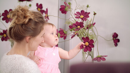 Obraz na płótnie Canvas Adorable baby touching flowers at home. Kid eating beautiful flowers in vase