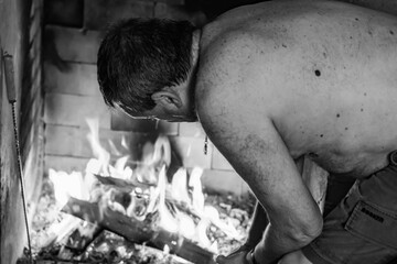 Hombre cuidando el fuego de un asado en blanco y negro