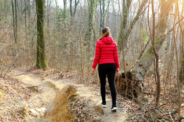 Young woman walking away alone on a forest path wearing a red down jacket in autumn winter