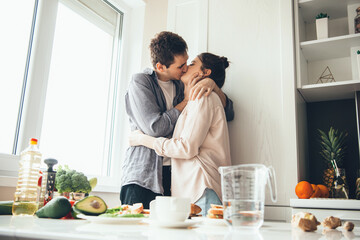 Fototapeta na wymiar Caucasian couple kissing in the kitchen while preparing food near the window