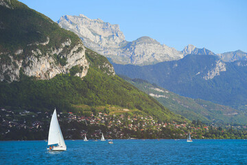 View of Annecy lake with clear turquoise water, sailing boats and traditional wooden houses in summer day, France