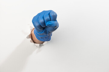 Fist in a latex glove kicking through torn white wall