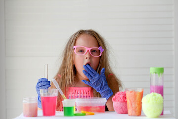 A little girl in pink glasses conducts experiments, looks at the camera . A child in rubber gloves...