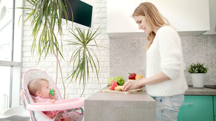 Mother cooking for baby on kitchen. Woman cooking with daughter in baby child