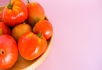 Red-yellow tomatoes on wooden plate on rose background with copy space