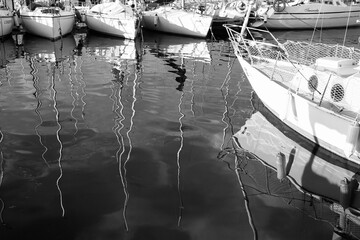 Fototapeta na wymiar Reflection of sailboats in the small harbor of Capodimonte Lazio Italy. Black and white photo.