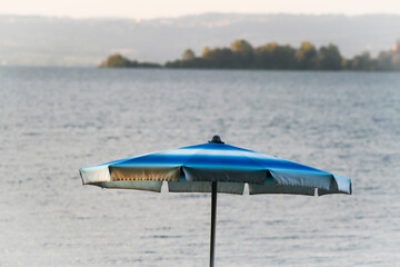 Blue sun umbrella in the foreground, in the background panorama of Lake Bolsena
